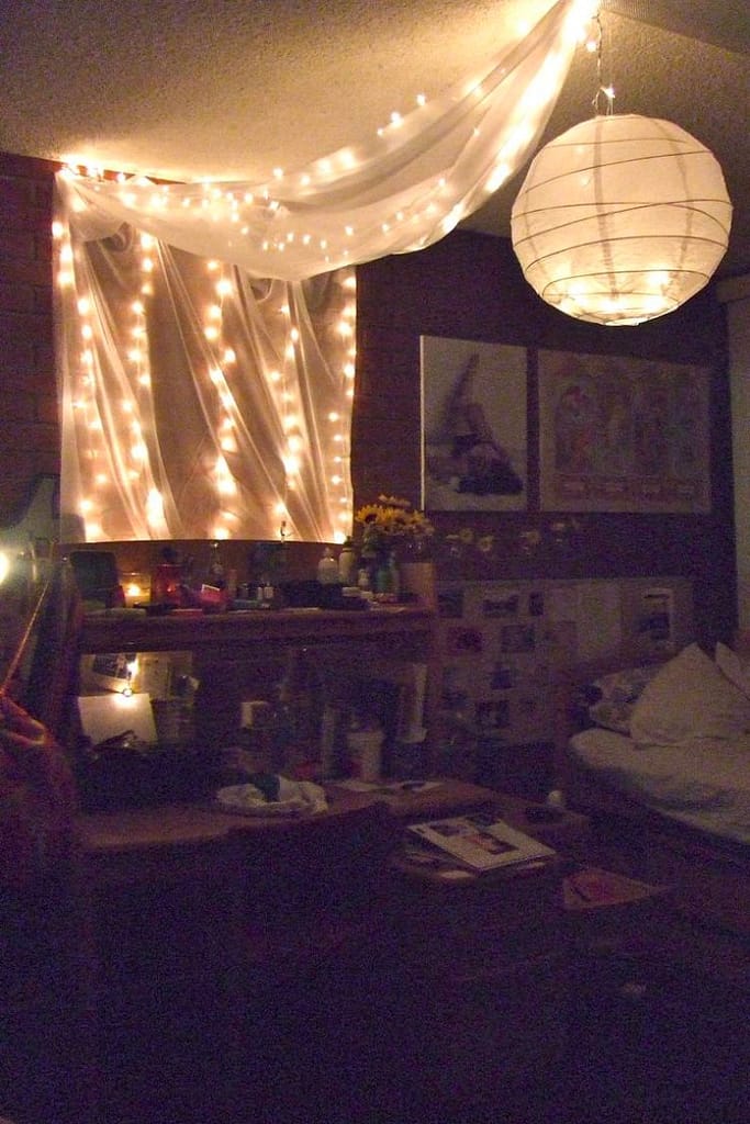 One paper lantern hanging from bedroom ceiling with string lights on the wall