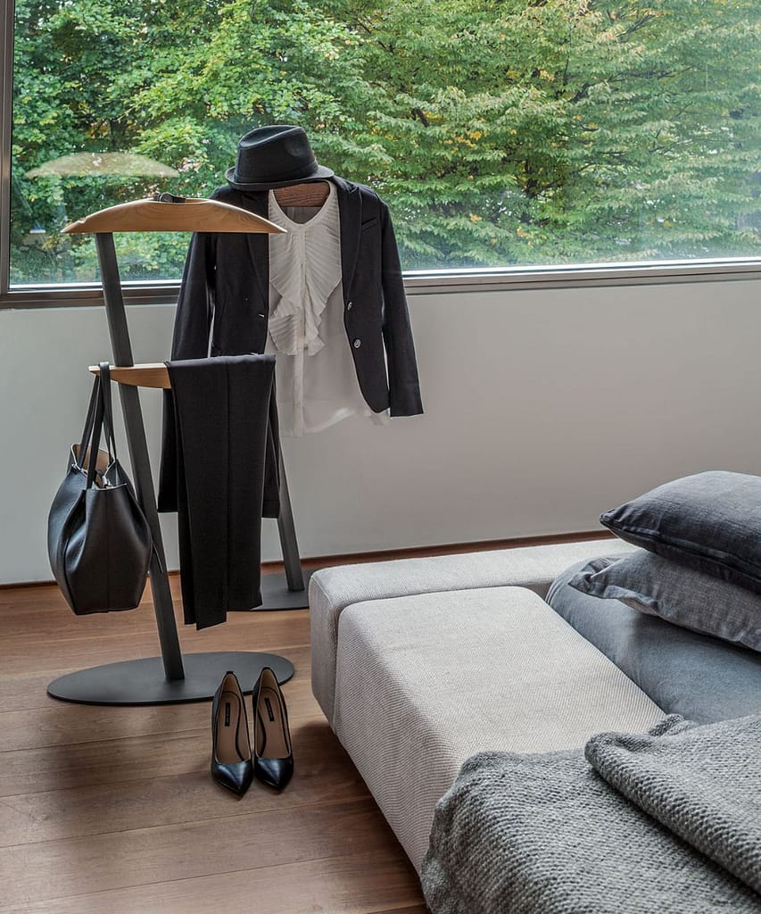 Valet stand with some clothes hanging on it next to a bed