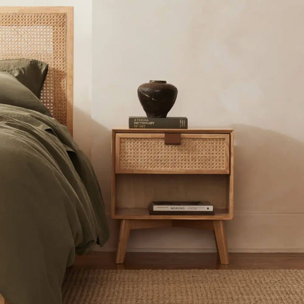 Rattan bedroom nightstand made of rubber wood next to a wooden bed frame with gray sheets